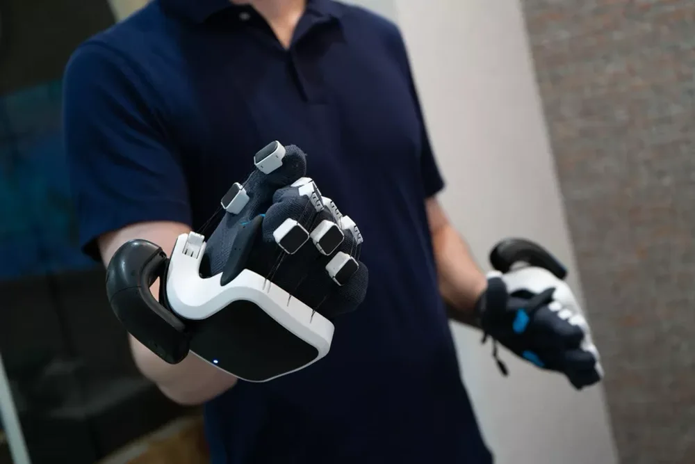 SenseGlove Nova 2 - Original Mogura VR photograph of SenseGlove Nova 2 gloves worn by a demonstrator, with mounted tracking controllers. Photograph from Ryota Musha's 31 October 2024 hands-on report.